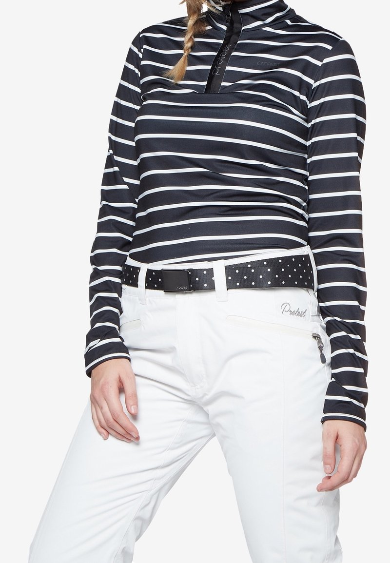 Persona che indossa una maglietta a righe orizzontali bianca e nera a maniche lunghe e pantaloni bianchi con una cintura nera decorata con pois bianchi.