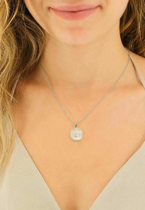 Collier pendentif en argent avec une forme irrégulière et une surface texturée, suspendu à une chaîne fine. Le pendentif présente un design détaillé.