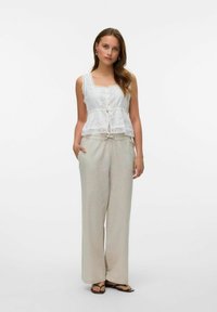 Haut en lin blanc avec bordure en dentelle et boutons, associé à un pantalon large beige clair, doté de poches et d'une coupe décontractée. Sandales en plastique marron.