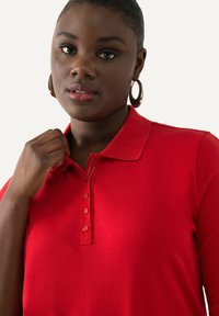 Camisa polo roja con cuello y detalles de botones. Tejido suave y liso con un color sólido y una forma ajustada.