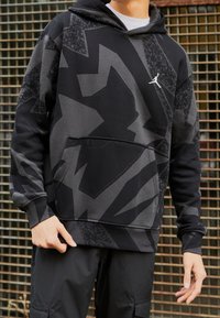 Sweat à capuche noir avec des motifs géométriques gris, poche avant et petit logo blanc sur la poitrine. Tissu doux et texturé.