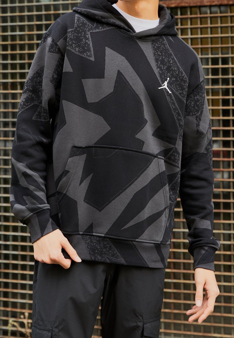 Sweat à capuche noir avec des motifs géométriques gris, poche avant et petit logo blanc sur la poitrine. Tissu doux et texturé.