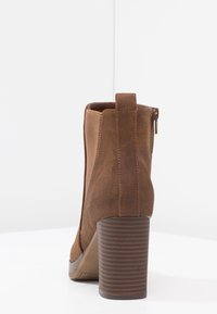 Brązowy zamszowy botek za kostkę z fakturowanym obcasem w kształcie bloku, z zamkiem i elastycznym panelem dla lepszego dopasowania. G�ładka podszewka wewnętrzna.