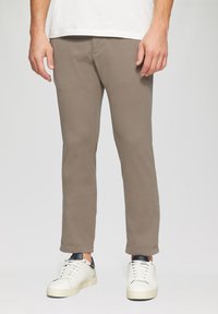 Pantalons chino en brun clair, fabriqués à partir de coton doux. Présentent une coupe slim, une jambe droite et un design minimaliste. Associés à des baskets blanches.
