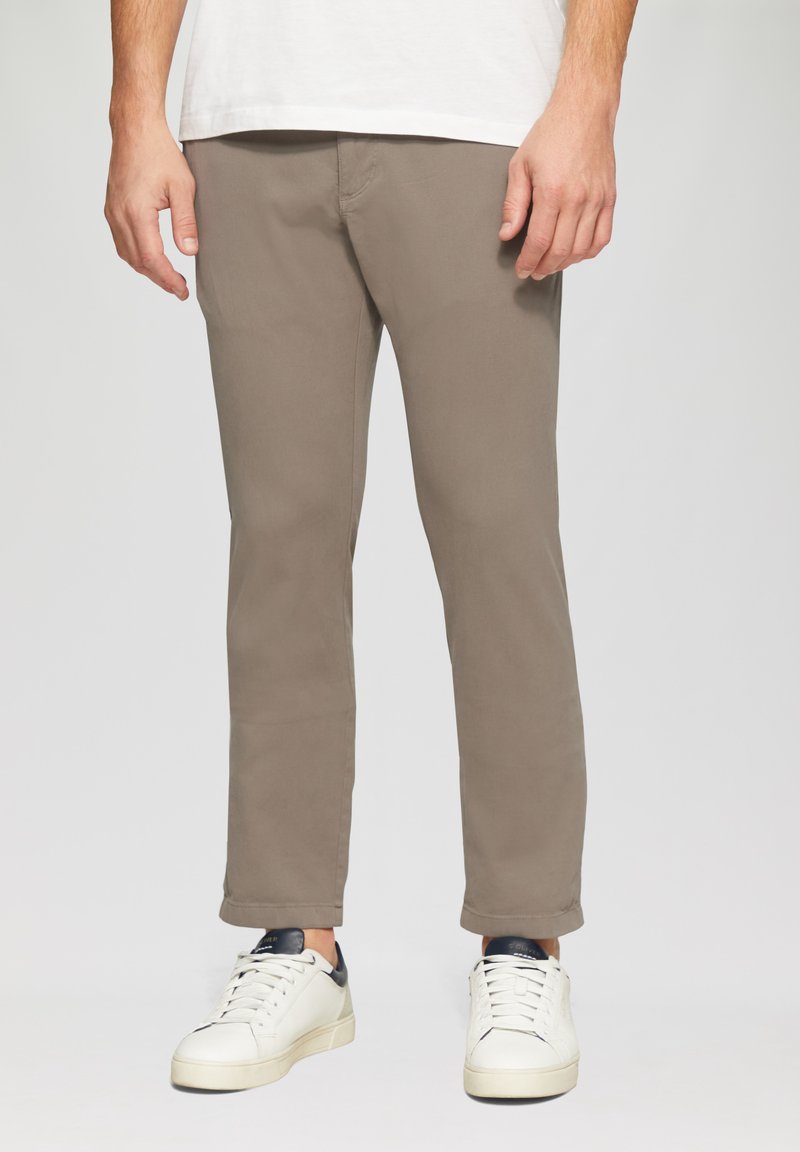 Pantalons chino en brun clair, fabriqués à partir de coton doux. Présentent une coupe slim, une jambe droite et un design minimaliste. Associés à des baskets blanches.