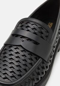 Sorteve svart vevet lær slip-on sko med et glatt lærbånd over foten. Har en teksturert overflate og en lavprofil gummisåle.