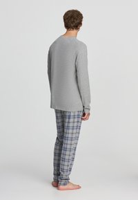 Maglietta grigia a maniche lunghe e pantaloni del pigiama a scacchi blu. La maglietta ha un colletto rotondo, mentre i pantaloni presentano un motivo a scacchi con risvolti alle caviglie.