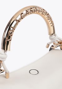 Vitt handväska med ett distinkt guldhandtag och präglad text "LOLA CASADEMUNT", som visar eleganta kurvor och en modern design.