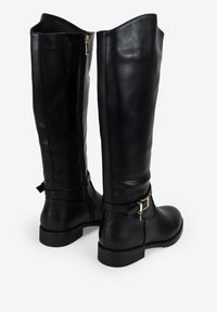 Botas de cuero negras hasta la rodilla con un acabado suave, cremalleras laterales y detalles de hebilla en tono dorado en las correas del tobillo. Suelas planas.