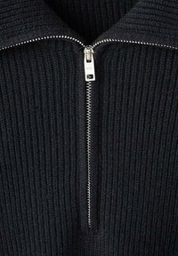 Maglione nero a costine con collo alto e zip argentata, che mette in risalto un tessuto testurizzato con linee verticali.