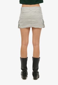 Grijze cargominirok met omgezoomde zoom, voorzien van zijzakken en achterzakken, gecombineerd met zwarte kniehoge laarzen.