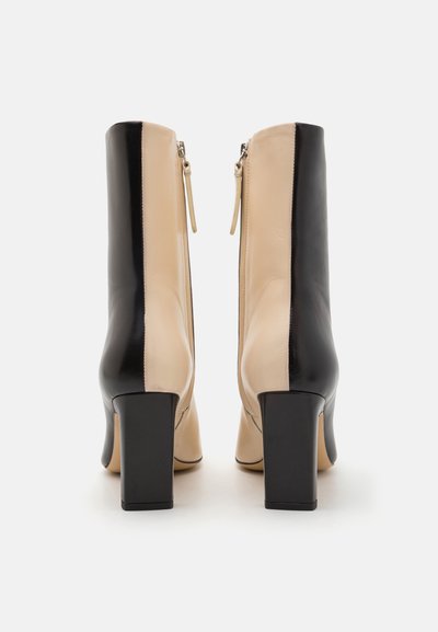 Leren enkellaarsjes met een bicolor ontwerp in beige en zwart, voorzien van een vierkante hak en ritssluitingen aan de zijkant.