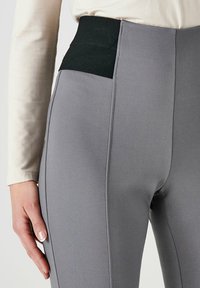Leggings gris avec une taille noire texturée, dotés de coutures plates pour une finition lisse et d'un design ajusté.