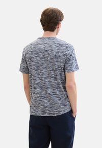 Short-sleeve t-shirt in a textured blue and gray pattern, featuring a crew neck and relaxed fit. Worn with dark pants.