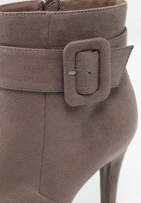 Stivaletto in suede grigio con una larga fascia e dettaglio della fibbia rettangolare, caratterizzato da un alto tacco a spillo e una texture liscia.