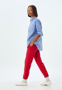 Blåstribet skjorte med knapper og opadvendte ærmer, parret med røde sweatpants og hvide sneakers. Casual fit, kontrasterende farver og slank design.