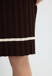 Bruine geribde rok met een horizontale witte streep near de zoom, getoond op het been van een persoon tegen een effen achtergrond.