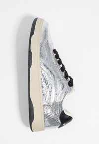 Silver sneaker with a textured metallic upper, black laces, cream midsole, and black accents at the heel and tongue.