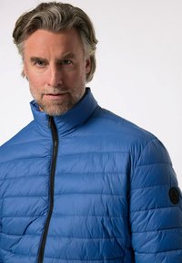 Modrá zateplená bunda s vysokým límcem, horizontálním prošíváním a zipovým zapínáním. Obsahuje černé kruhové logo na rukávu.