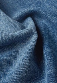 Tessuto di denim di colore blu medio, con una classica tessitura a spina di pesce, che mostra variazioni di trama e una leggera scoloritura naturale.