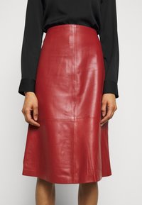 Falda midi de cuero rojo con una textura suave, cintura ajustada y detalles de costura. Estilizada con una blusa negra de manga larga.
