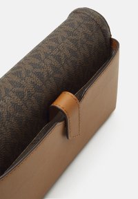 Braune Ledertasche mit einem Klappdeckel im geometrischen Muster. Sie verfügt über ein glattes, strukturiertes Design und einen kleinen Riemen zum Verschließen. Die Oberfläche des Klappdecks ist strukturiert.