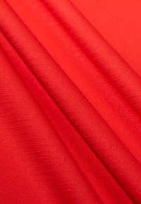 Tessuto rosso con una consistenza liscia, che mostra una leggera lucentezza e un motivo a righe diagonali. Il materiale è piegato, mettendo in risalto il suo colore vivace.