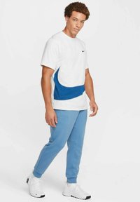 White short-sleeve t-shirt with blue accent, paired with light blue sweatpants and white sneakers. Features a round neckline and a relaxed fit.