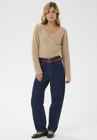 Bež pulover s puhastim videzom in dolgimi rokavi, v kombinaciji z temno modrimi kavbojkami z visokim pasom in rjavim usnjenim pasom. Črne balerinke dopolnjujejo obleko.