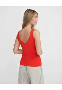 Top in tessuto a coste rosso con scollatura a V profonda, caratterizzato da spalline larghe e un design aderente. Il modello lo abbina a pantaloni a righe.