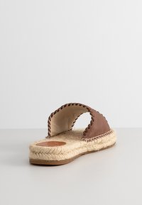 Brown leather upper with braided stitching, jute rope sole, flat design. Open-toe with a wide strap across the top.