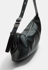 Schwarze Lederhandtasche mit geschwungener Form, ausgestattet mit einem silbernen Reißverschluss und einem verstellbaren Tragegurt mit einer Schnalle. Texturiertes, sanft gerafftes Design.