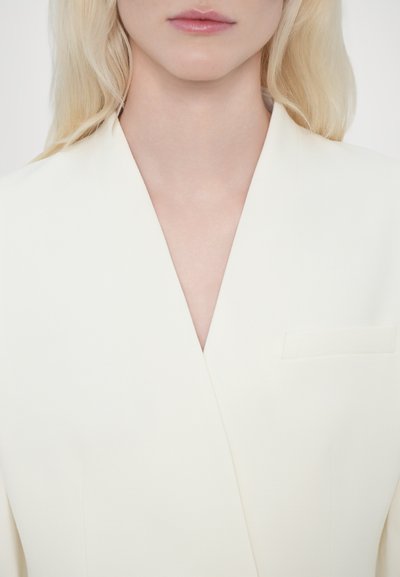 Witte blazer met een diepe V-hals en een enkel borstzakje. Glad, gestructureerd materiaal zorgt voor een cleane silhouette.
