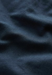 Tissu bleu foncé avec une texture apparente de tissage diagonal fin et des plis naturels créant des ombres et des reflets doux.