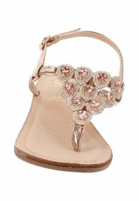 I sandali color oro rosa presentano un design con cinturino a T decorato con strass rosa a forma di cuore e una soletta beige testurizzata. Cinturino alla caviglia regolabile.