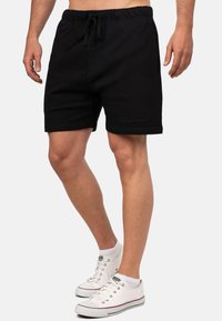 Zwarte shorts met trekkoord, gemaakt van een zachte katoenmix, met gestikte details en een ontspannen pasvorm, gecombineerd met witte sneakers.