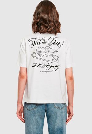 T-shirt en coton blanc à manches courtes, avec un grand graphique noir au dos représentant une épingle à nourrice et des cœurs, accompagné de texte.