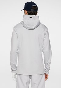 Hellgrauer Hoodie mit Kapuze zum Zuziehen, langen Ärmeln und einem Logo auf der Rückseite. Aus einem glatten Stoff gefertigt mit taillierter Passform.