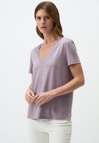 T-shirt scollato a maniche corte di un delicato colore viola, realizzato in tessuto morbido, con una vestibilità comoda e una superficie liscia, abbinato a pantaloni bianchi.