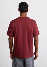 T-shirt di cotone bordeaux con maniche corte, collo rotondo e vestibilità comoda. Texture liscia e design sul retro semplice senza loghi o motivi.