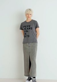 Camiseta gris con "PEPE JEANS SINCE 1973" impreso en negro, combinada con una falda maxi de mezclilla gris con una abertura frontal y zapatillas negras.