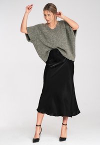 Przesadzony, teksturowany szary sweter z dekoltem w serek, w połączeniu z czarną satynową spódnicą midi i czarnymi szpilkami.