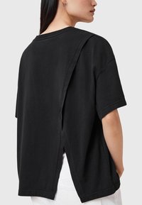 T-shirt nera oversize con design a schiena aperta, maniche corte e colletto rotondo. Realizzata in cotone con una texture morbida.
