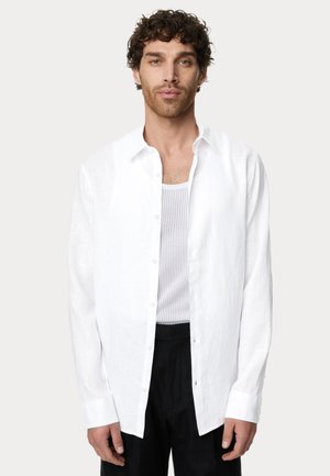 Witte linnen knopsluiting shirt met lange mouwen, open kraag en een losse pasvorm, gelaagd over een witte mesh tanktop.