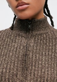 Brązowy, prążkowany sweter na zamek z wysokim kołnierzem i teksturowanym wzorem dzianiny; czarne zamki błyskawiczne; zbliżenie na linię szyi.