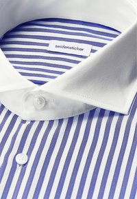 Camicia a righe blu e bianche con colletto bianco, caratterizzata da una patta con bottoni e l'etichetta "seidensticker" all'interno. Tessuto in cotone.