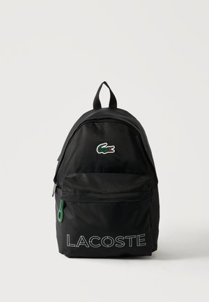 Sac à dos noir Lacoste avec poche avant zippée, tirette verte et logo crocodile vert au-dessus du texte blanc "LACOSTE".