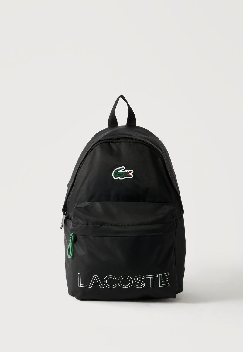 Μαύρο σακίδιο πλάτης Lacoste με μπροστινή τσέπη με φερμουάρ, πράσινη τσόχα φερμουάρ και πράσινο λογότυπο κροκόδειλου πάνω από λευκό κείμενο "LACOSTE".