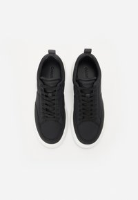 Baskets noires avec un dessus en textile lisse, dotées de lacets ton sur ton et d'une semelle en caoutchouc blanche. Le logo de la marque est en relief sur la languette.