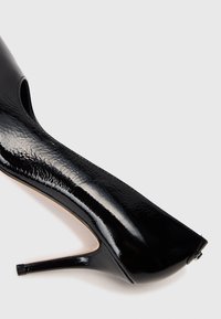 Črna sijajna stiletto petka je prikazana s strani na preprosti beli podlagi.
